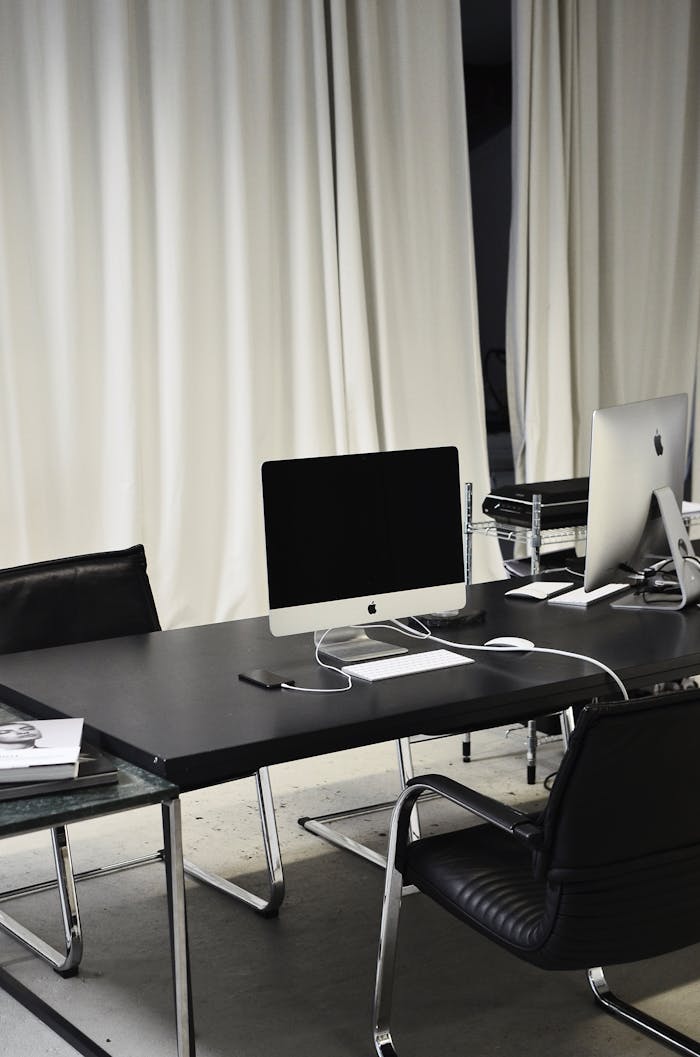 Black and white of computer with wireless keyboard and mouse placed on table near smartphone on charge in business office